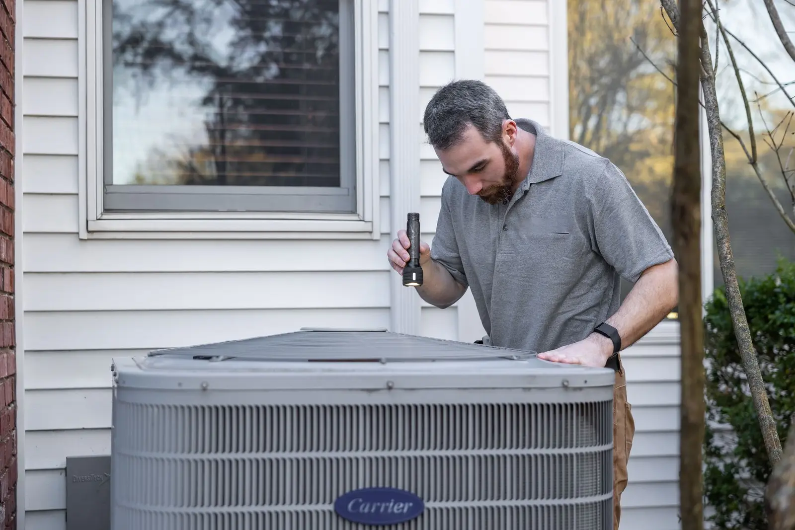 Technician inspecting a residential outdoor air conditioner. HVAC marketing for peak season and the quiet weeks