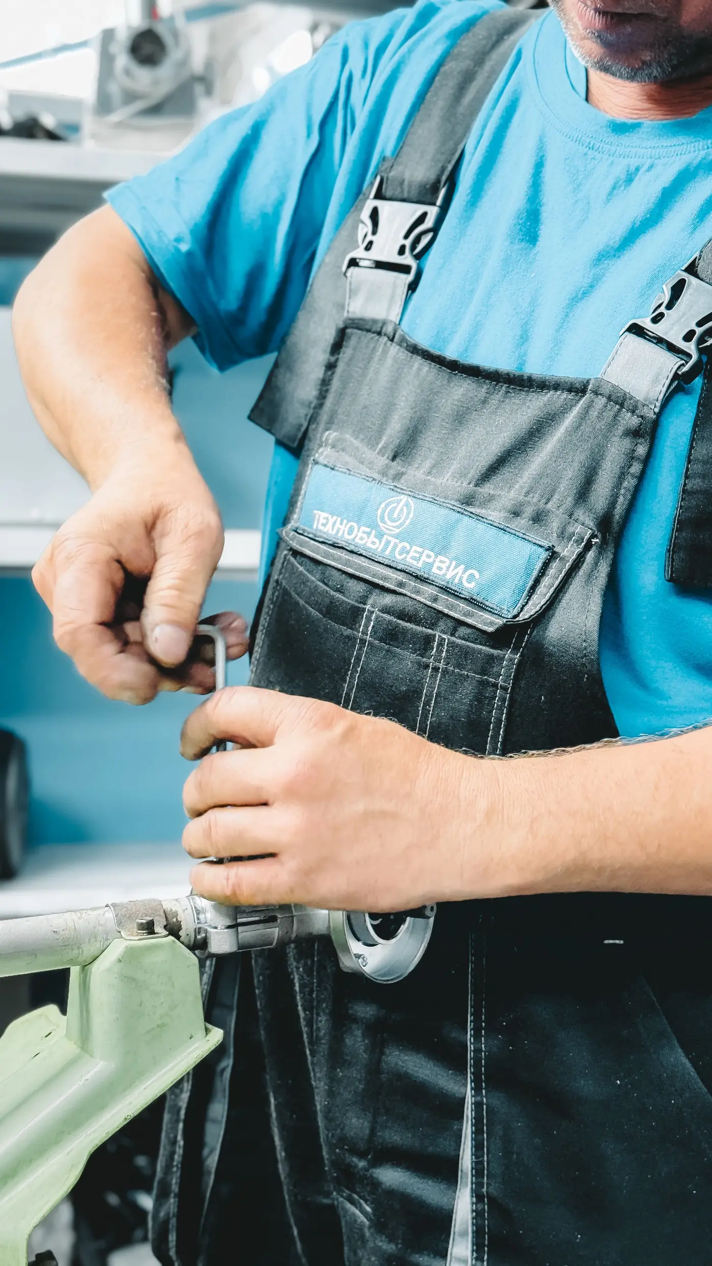 Plumber in blue coveralls repairing a pipe with a wrench. Plumbing marketing for emergency calls and planned work